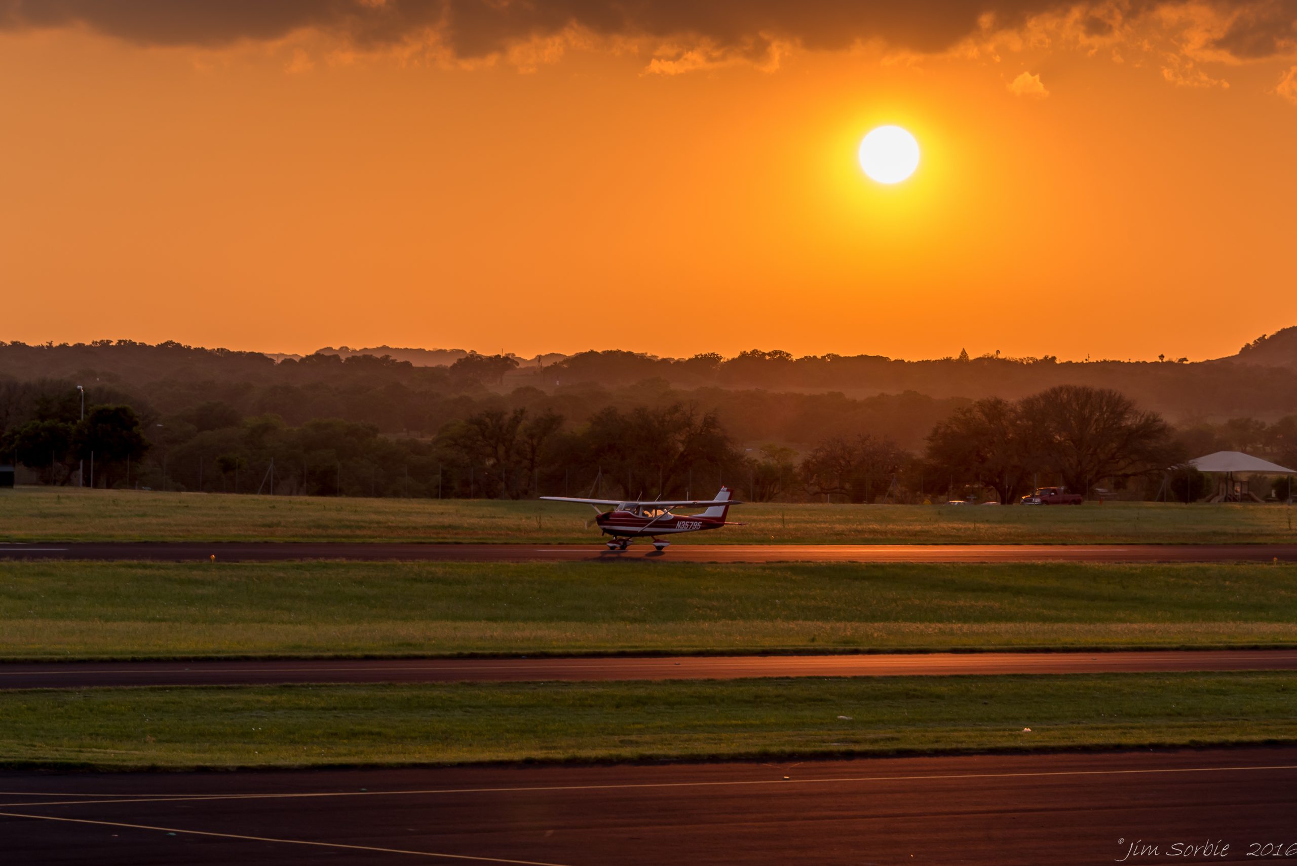 Small aircraft taxiing at sunset on a rural Texas airport runway with rolling hills in the background